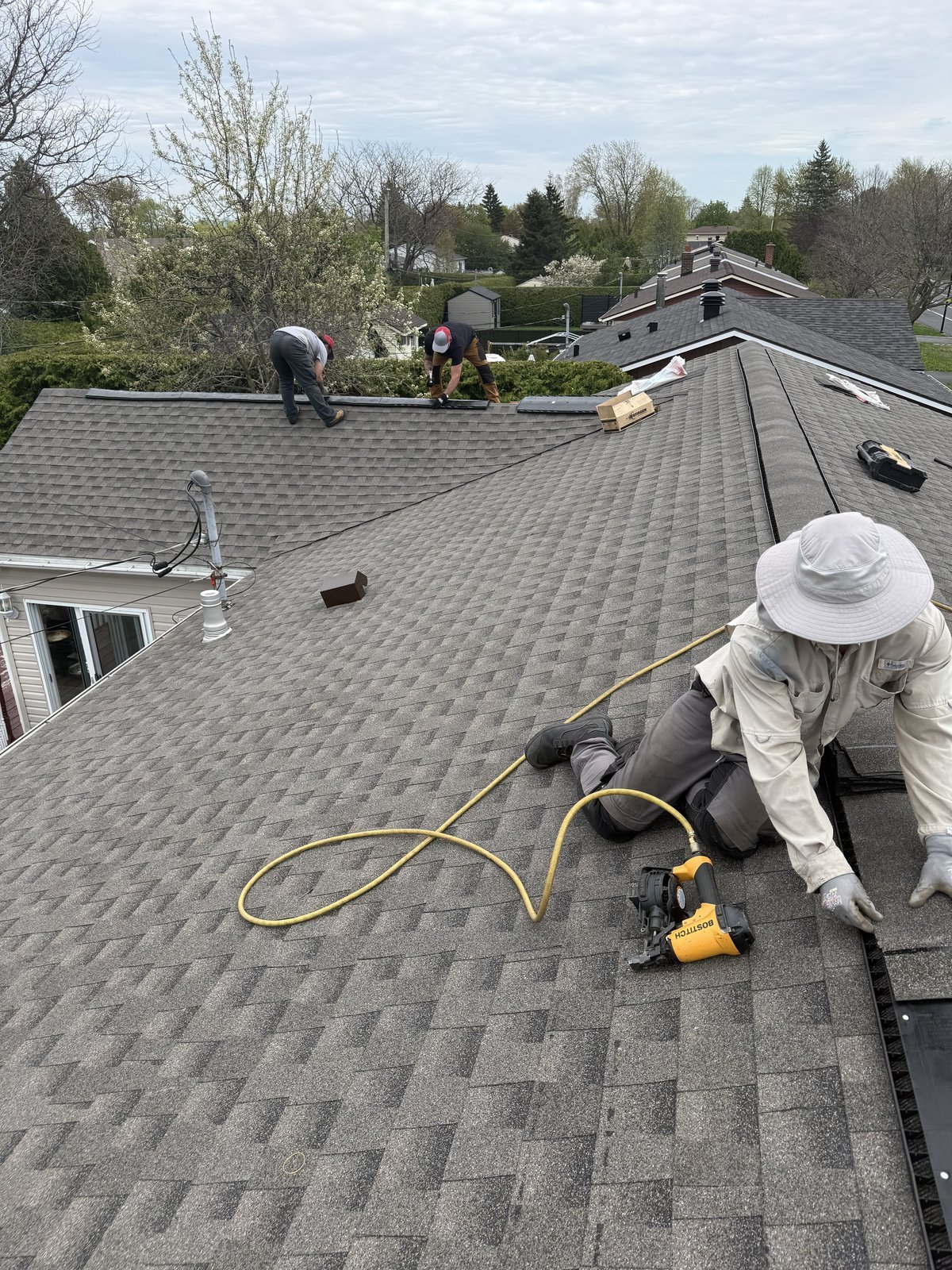 Couvreurs de Construction Montéa installant les bardeaux et la ventilation de faîte sur une toiture résidentielle